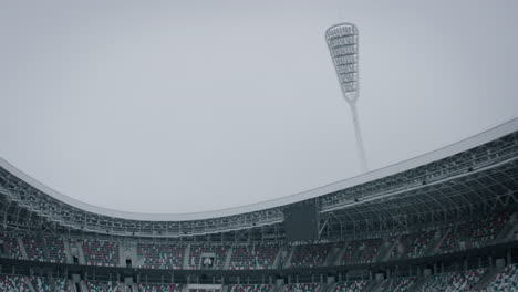 Empty-outdoor-football-soccer-stadium-seats-covered-with-snow-in-winter,-light-snowfall.-Shot-with-2x-anamorphic-lens.-120-FPS-Slow-motion